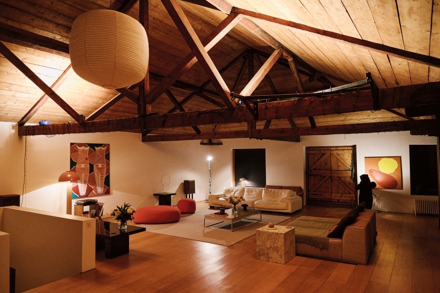Spacious loft with wooden vaulted ceiling, modern furniture, artwork, and warm lighting.