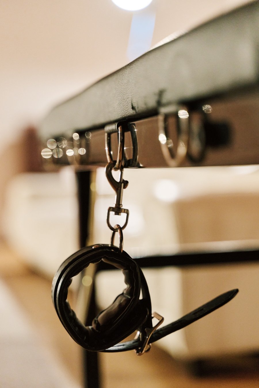 Black leather strap with metal buckle hanging from metal hooks under a black surface.